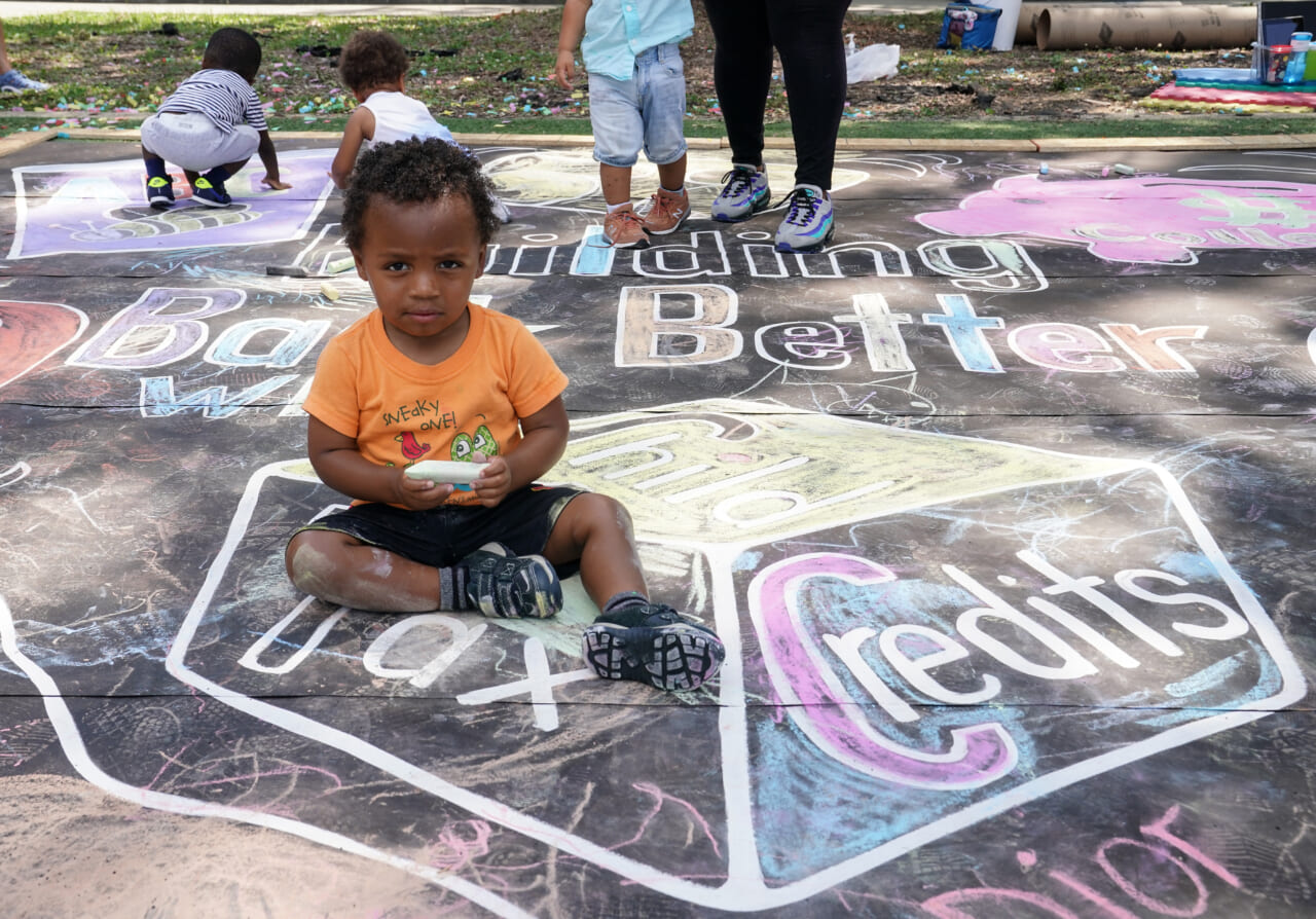 A child sitting on a chalk mural on the sidewalk