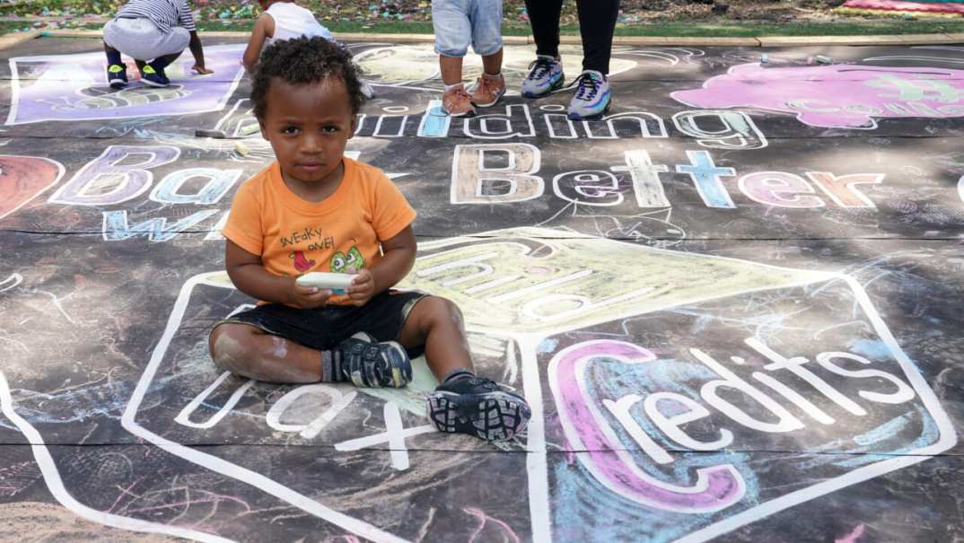 A child sitting on a chalk mural on the sidewalk