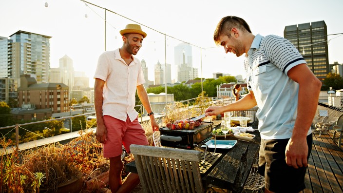 Two men cook shish kebabs on a tabletop grill