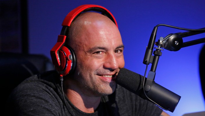 Podcaster Joe Rogan at a microphone wearing red headphones and a black shirt