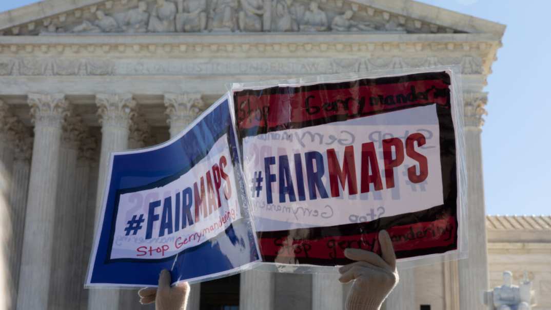 A set of hands holds up signs reading "#FairMaps - Stop Gerrymandering"