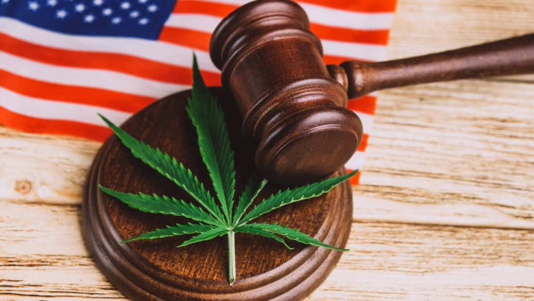 An American flag behind a gavel and a sound block with a marijuana leaf