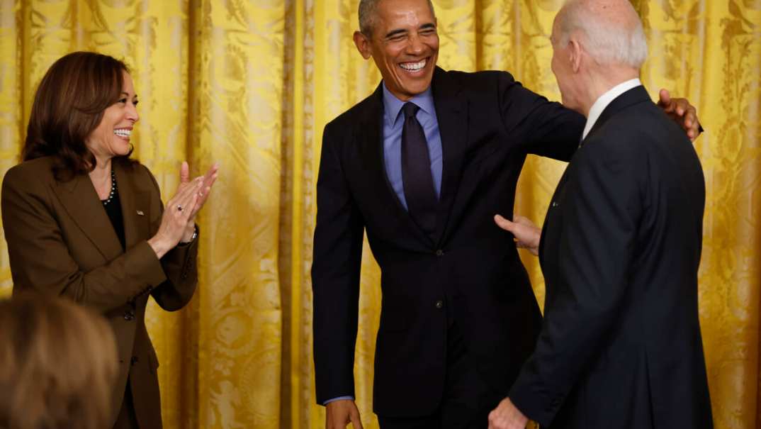 Vice President Kamala Harris applauds beside former President Barack Obama who reaches toward President Joe Biden