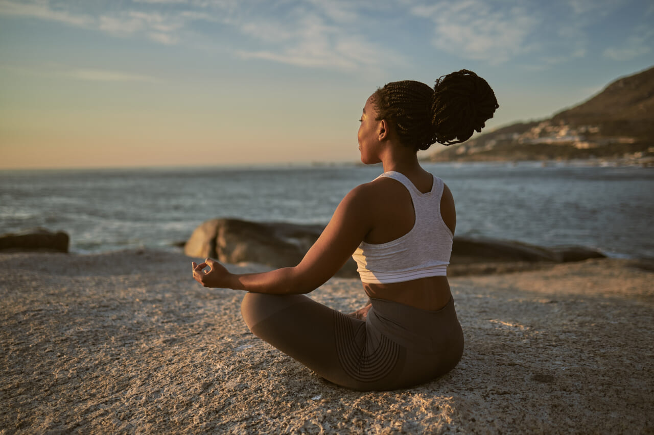 A woman sits in lotus position on a beach