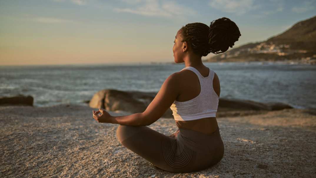 A woman sits in lotus position on a beach