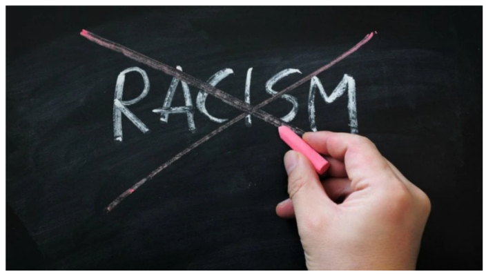 A hand crosses out the word "Racism" on a chalkboard