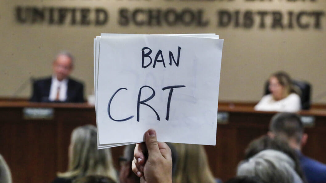 A hand holding a sign reading "Ban CRT"