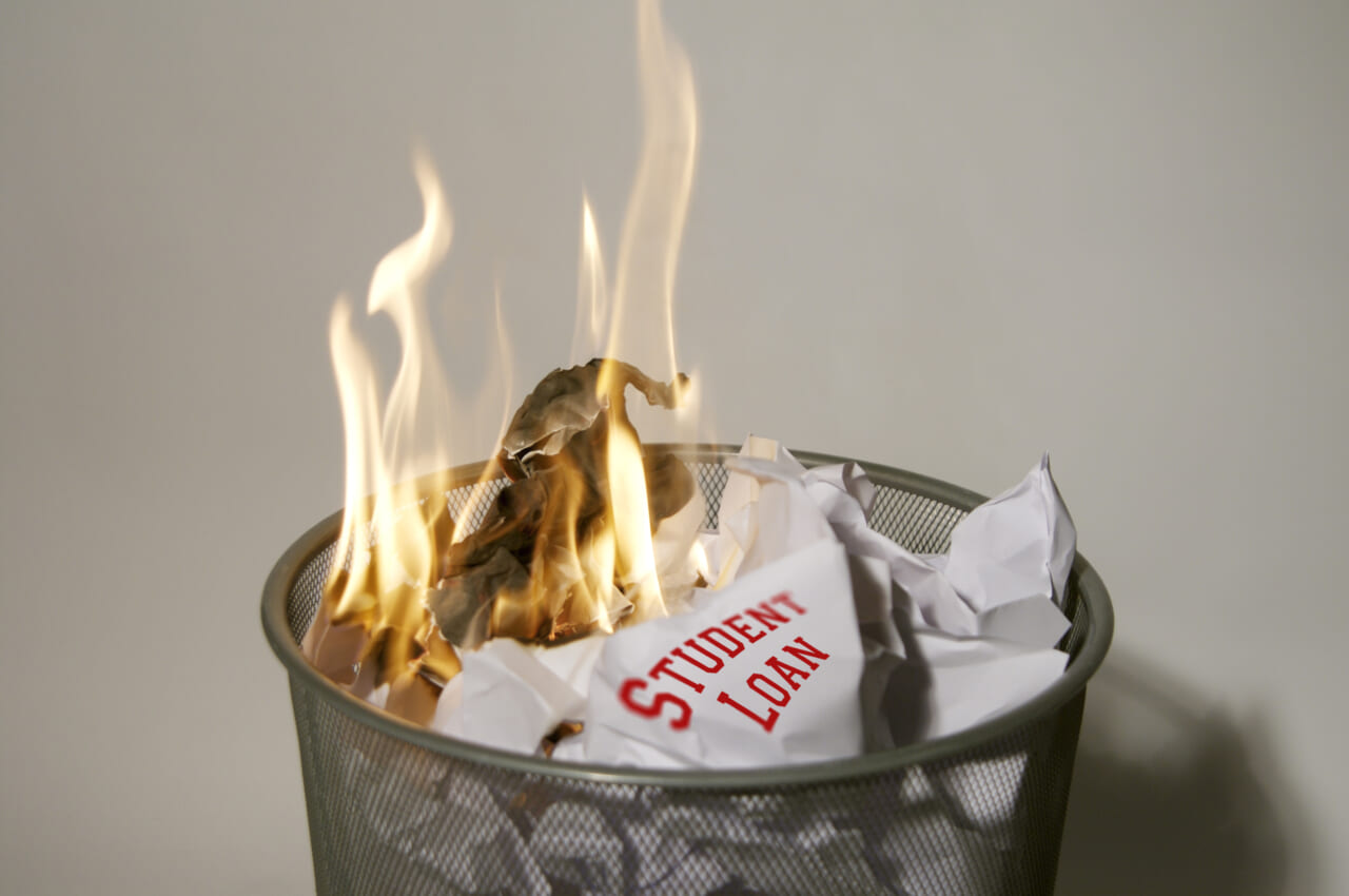 A paper reading "Student Loan" burning in a wastebasket