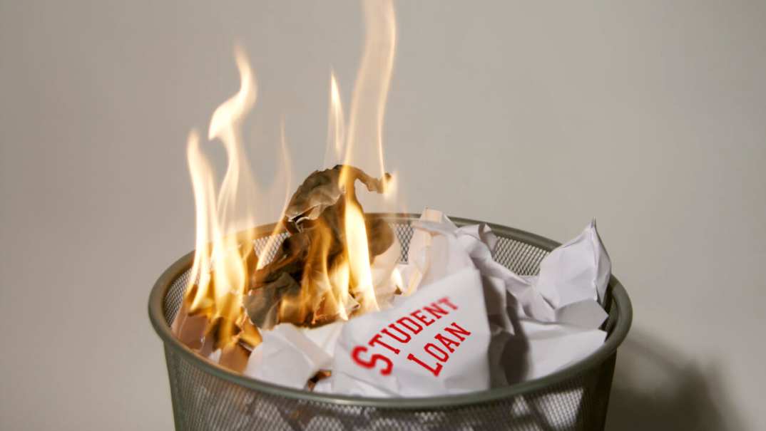 A paper reading "Student Loan" burning in a wastebasket