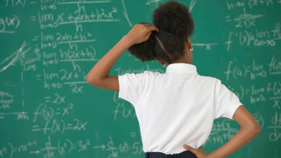 A girl stands at a chalkboard scratching her head