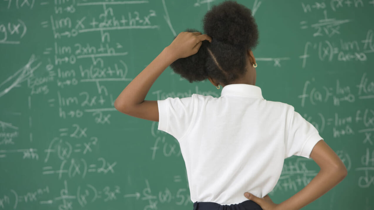 A girl stands at a chalkboard scratching her head