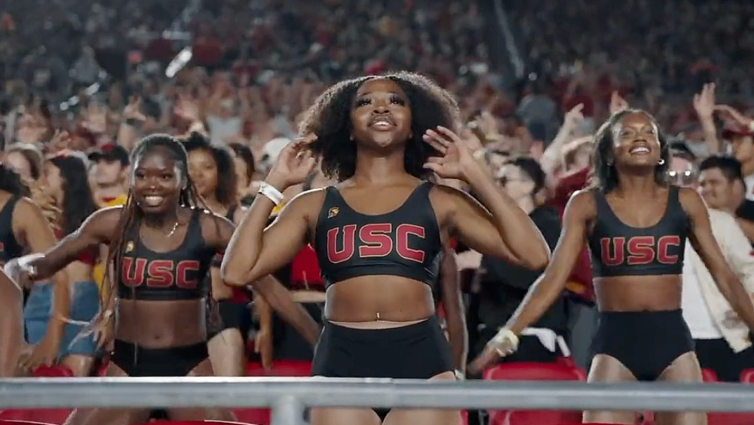 The Cardinal Divas perform in the stands at a sports game, wearing black two-piece outfits