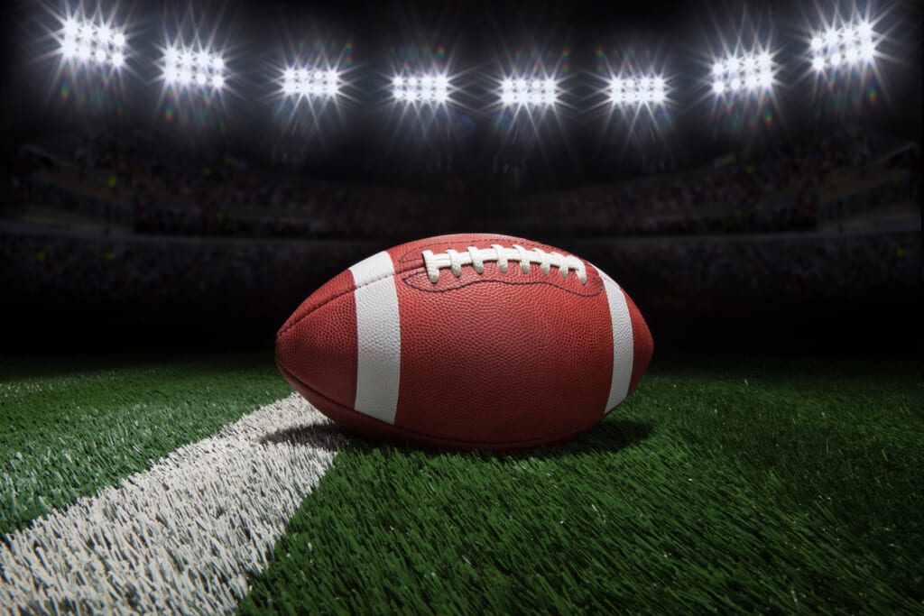 College style football on a yard line of a football field under stadium lights