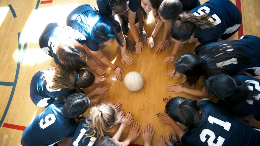 Young people kneel on a basketball court around a volleyball