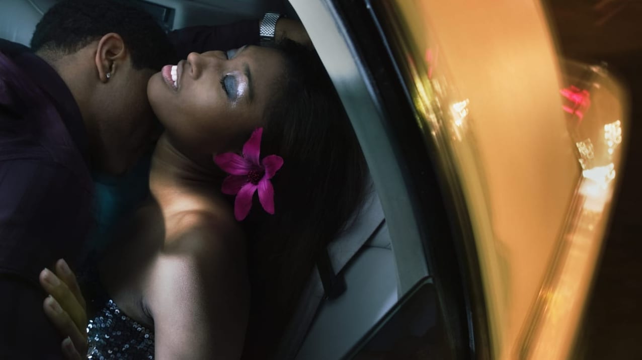 A man kisses a woman on the neck in a car