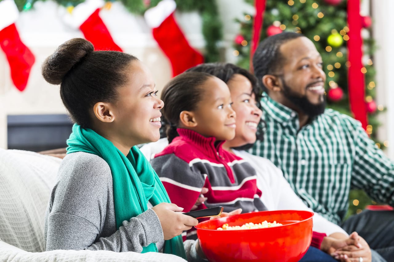 A family sits on a couch with a bowl of popcorn, smiling