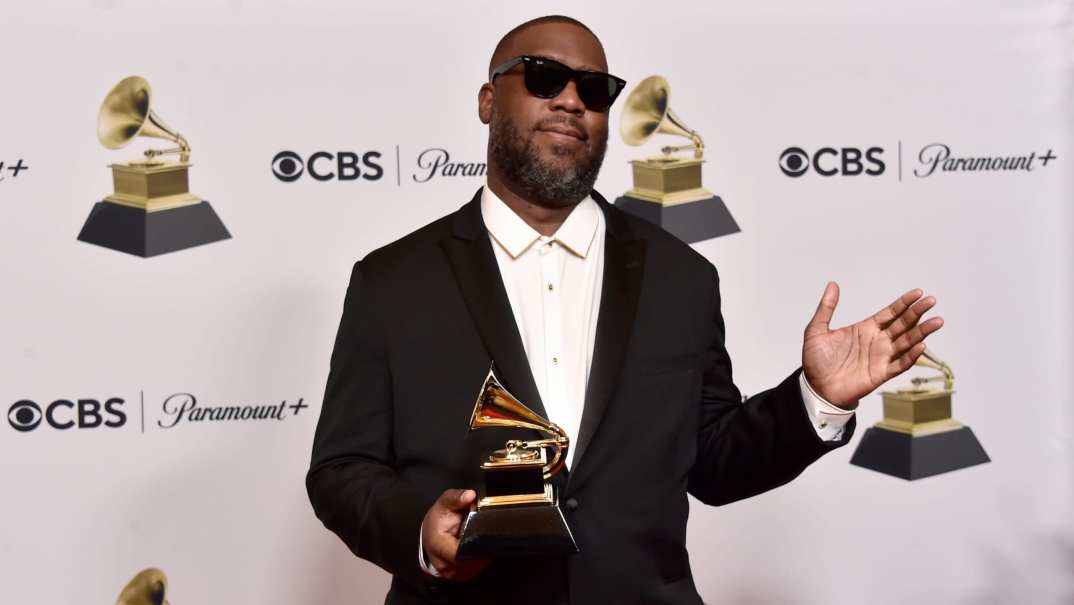 Rapper Robert Glasper holding his Grammy award, wearing a white shirt and black jacket