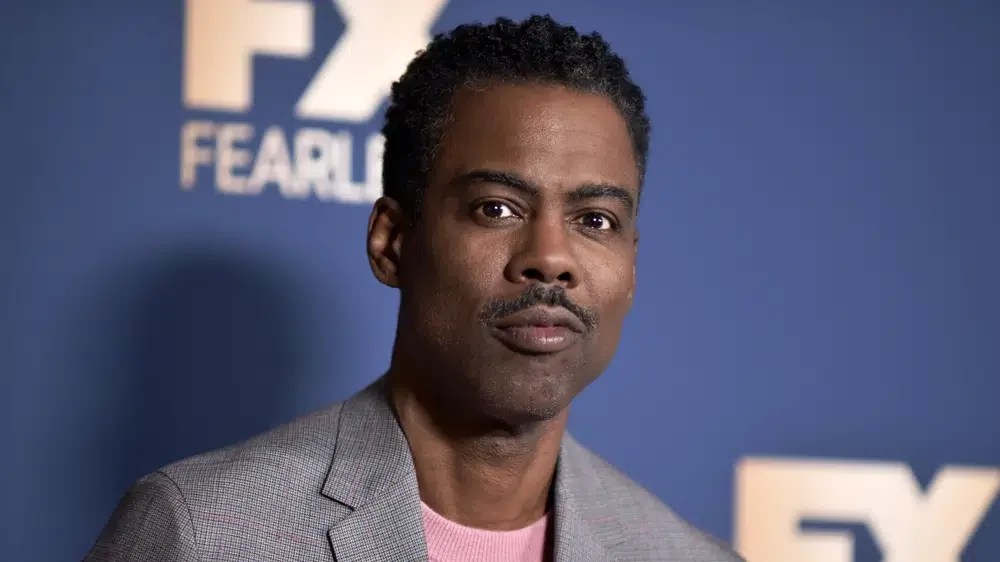 Actor and comedian Chris Rock wearing a gray checked jacket and pink shirt