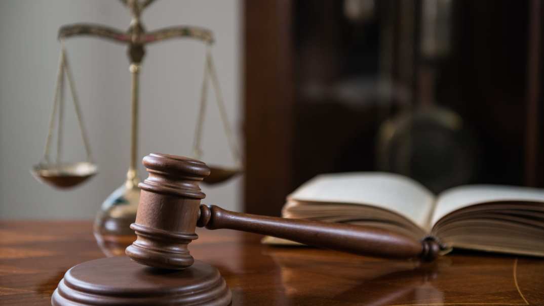 A wooden table displays a brown wooden gavel and sound block, an open book and a brass scale