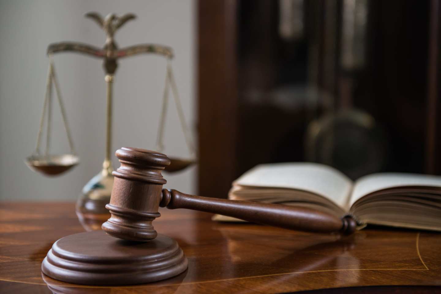 A wooden table displays a brown wooden gavel and sound block, an open book and a brass scale