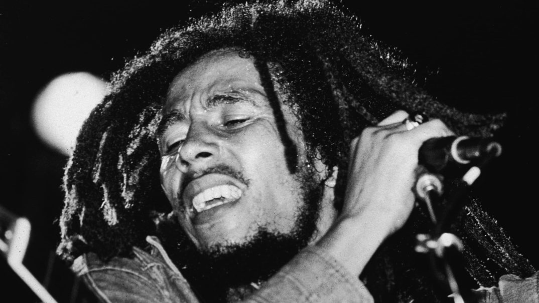 Black-and-white photo of the late Jamaican reggae musician Bob Marley on stage with a microphone in the late 1970s.