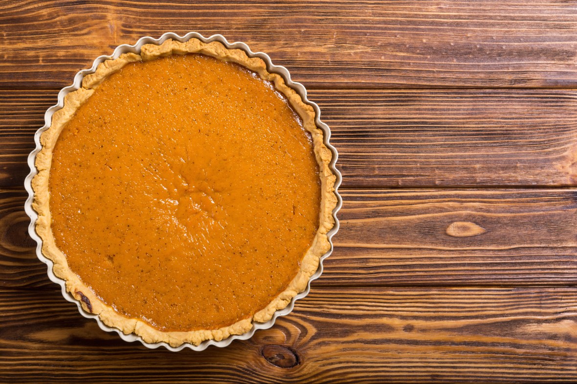 A pumpkin pie sitting on a wood table - aerial shot.