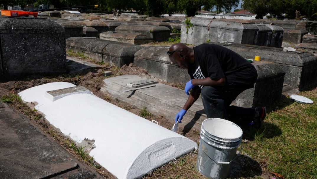 Frank Wooden, dressed in black, paints a grave white at the Lincoln Memorial Park Cemetery in Miami