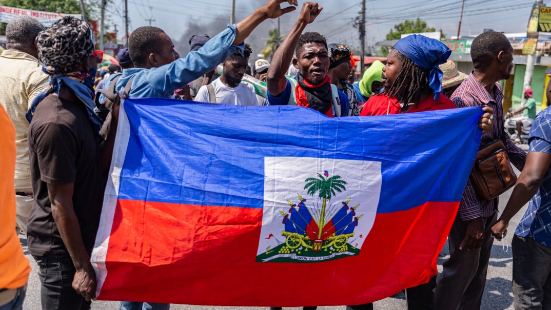 A group of people hold a Haitian flag and raise their hands in the air