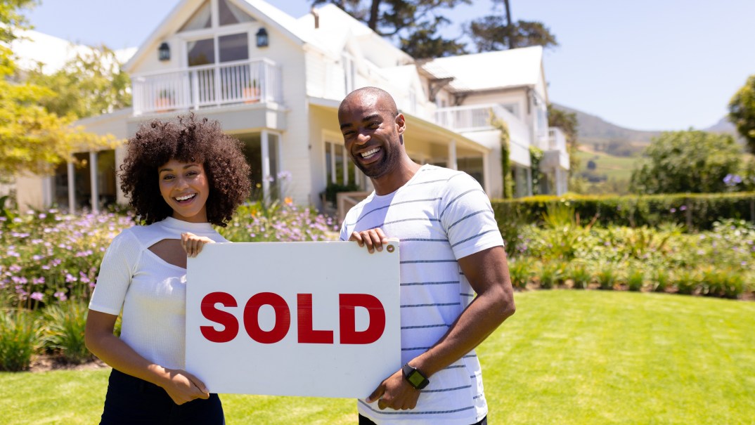 A couple in front of a house holding a "Sold" sign