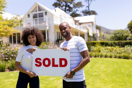 A couple in front of a house holding a "Sold" sign