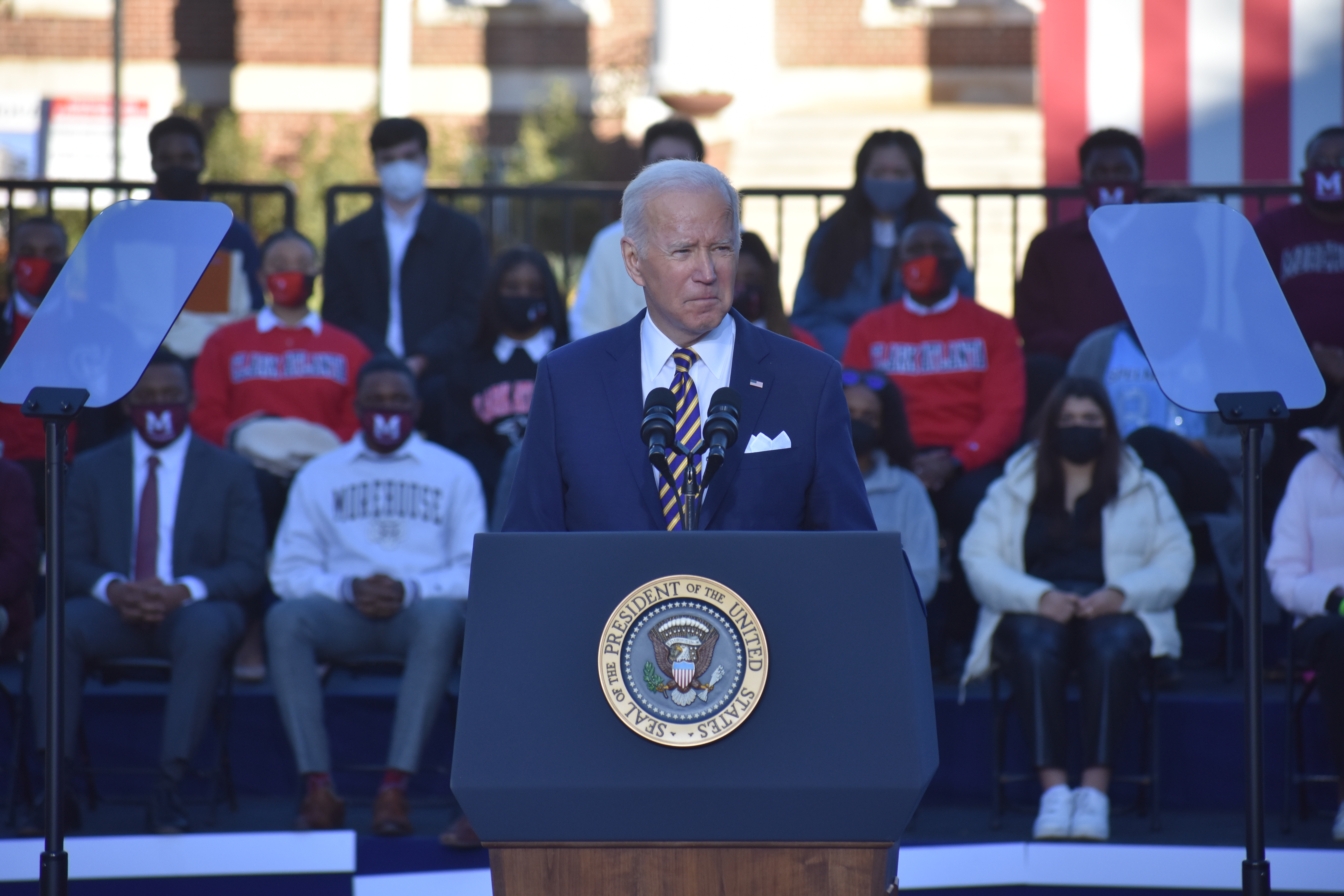 President Joe Biden in a blue suit and blue-and-yellow striped tie behind a podium