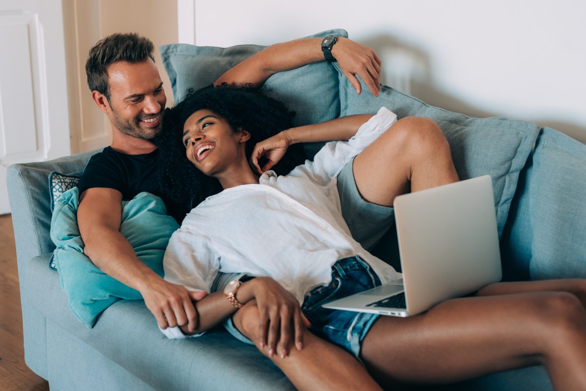 A couple lays together on a couch with a laptop