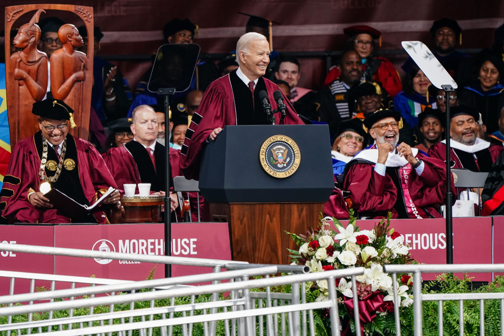 President Joe Biden stands behind a podium wearing a dark red graduate robe over a black suit and red tie