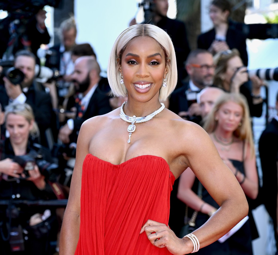 Singer and actor Kelly Rowland poses wearing a red strapless dress and silver necklace