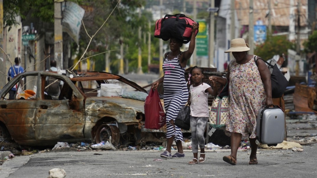 Residents walk past a burnt car blocking the street