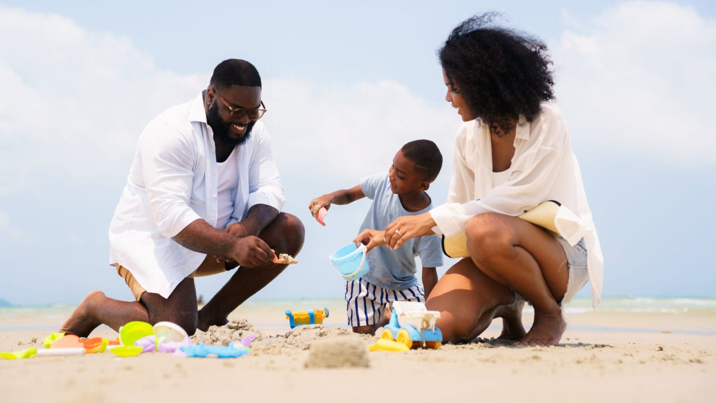 Happy Black family building sandcastle together on beach